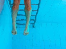Piernas de mujer europea caucásica blanca adulta con pedicura ultravioleta naranja bajo el agua en la piscina. verano. graciosas piernas submarinas en concepto de piscina, vacaciones y deporte. foto