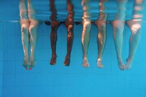 Legs of African American man with caucasian friends in swimming pool underwater. Summer. Vacation, international and sport concept. photo