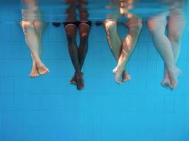 Legs of African American man with caucasian friends in swimming pool underwater. Summer. Vacation, international and sport concept. photo