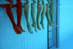 Legs of African American man with caucasian friends in swimming pool underwater. Summer. Vacation, international and sport concept. photo