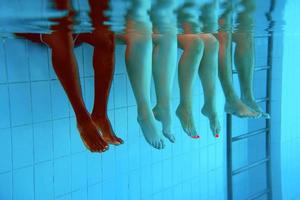 Legs of African American man with caucasian friends in swimming pool underwater. Summer. Vacation, international and sport concept. photo