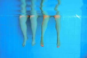 piernas de dos personas bajo el agua en la piscina. fiesta. verano. concepto de vacaciones, diversidad, amistad y deporte. foto