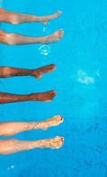 legs of four friends different race sitting by the swimming pool in sunny day. Party. Summer. Vacation, international friendship and sport concept. photo