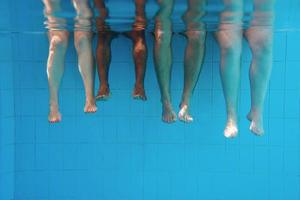 Legs of African American man with caucasian friends in swimming pool underwater. Summer. Vacation, international and sport concept. photo