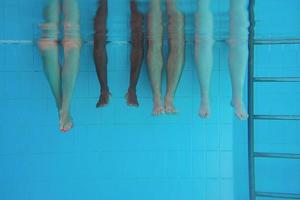 piernas de hombre afroamericano con amigos caucásicos en piscina bajo el agua. verano. concepto de vacaciones, internacional y deportivo. foto
