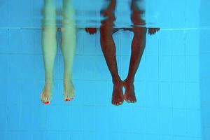 adult African American man's legs and caucasian woman legs underwater in swimming pool. Sport, recreation, vacation and friendship concept photo