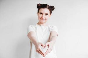 Portrait of beautifull woman making a heart shape with her fingers standing over white backgrounnd. Copy, empty space photo