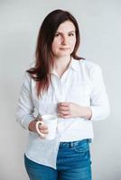 Beautiful woman in a white shirt holding a white ceramic cup on a white background. Woman drinking water coffee tea from white mug cup. Copy, empty space for text photo