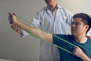 cierre el paciente de la mano haciendo ejercicio de estiramiento con una banda de ejercicio flexible y una mano de fisioterapeuta para ayudar en la sala de la clínica. foto