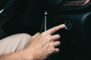 The man hand is holding a beer bottle and pressing the engine start button. photo