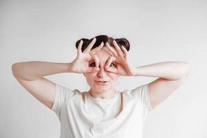 Portrait of a beautiful woman with her hands emitting glasses and a funny face wearing a T-shirt on a white background. Copy, empty space photo