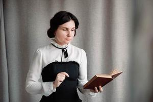 retrato de una mujer vestida de estilo vintage sosteniendo un libro en sus manos sobre un fondo de tela de lino foto