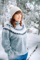 bella mujer con un gorro cálido y un suéter sobre un fondo de bosque nevado foto