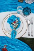 White banquet table covered with blue cloth, served with plates, cutlery, glasses, candles and flower arrangements. Top view. Copy, empty space for text photo