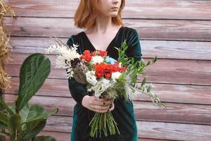 Beautiful girl in a green dress holding a bouquet of flowers and greenery on a wooden background. Copy, empty space for text photo