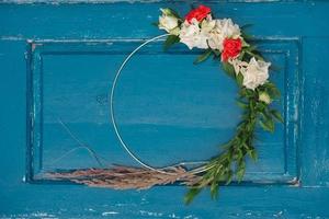 Decorated wreath of flowers, leaves and dry grass on a wooden blue door background. Copy, empty space for text photo