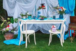 White banquet table covered with blue cloth, served with plates, cutlery, glasses, candles and flower arrangements. Copy, empty space for text photo