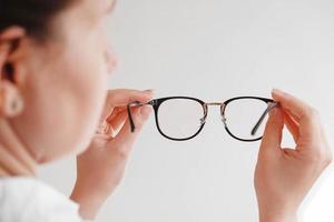 Woman holding optical glasses in a black frame on a white background. Copy, empty space photo