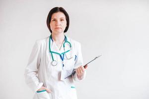 Friendly female doctor in a white coat with a folder in his hands and a stethoscope on a white background photo