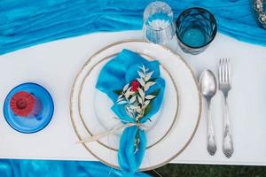 White banquet table covered with blue cloth, served with plates, cutlery, glasses, candles and flower arrangements. Top view. Copy, empty space for text photo