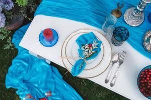 White banquet table covered with blue cloth, served with plates, cutlery, glasses, candles and flower arrangements. Top view. Copy, empty space for text photo