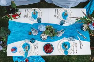 White banquet table covered with blue cloth, served with plates, cutlery, glasses, candles and flower arrangements. Top view. Copy, empty space for text photo