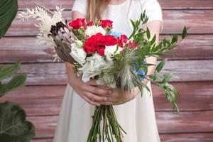 Beautiful girl in a green dress holding a bouquet of flowers and greenery on a wooden background. Copy, empty space for text photo