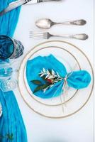 White banquet table covered with blue cloth, served with plates, cutlery, glasses, candles and flower arrangements. Top view. Copy, empty space for text photo