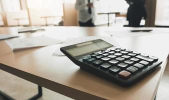 Close up of calculator on desk with business people talking background. photo