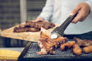 Asian men are pinching the pork ribs on the grill and holding them to friends who are celebrating in the back. photo