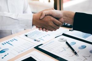 Entrepreneurs collaboration deal shaking hands in a modern office and financial paper graph on desk. photo