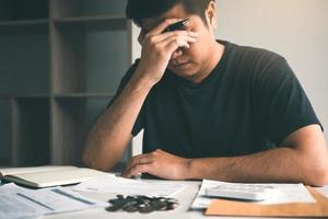 los hombres asiáticos están estresados por problemas financieros, con facturas y calculadoras colocadas sobre la mesa mientras tienen estrés por problemas con los gastos del hogar. foto