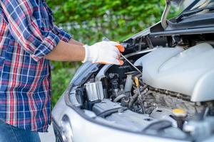 Asian auto mechanic check for repair under the hood of broken down car on the side of the road. photo