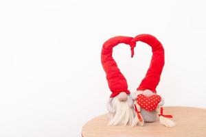 Two gnomes in love in red caps with a heart shape on a white background with copy space photo