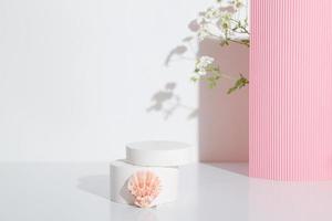 Empty cylindrical podium or plinth with chamomile flowers and seashell on white background. Blank shelf product standing background photo