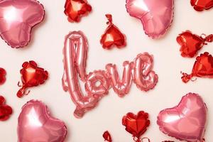 Festive background for Valentines Day from foil balloons shape heart and love word on beige background top view photo