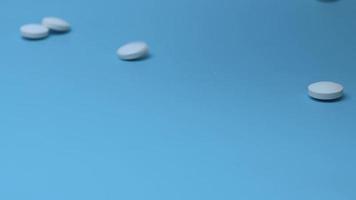 tabletter faller på en blå bakgrund och rullar på bordet. begreppet medicin och missbruk. video