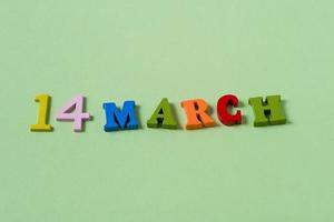 14 de marzo, diseño de portada de fecha con letras k de madera multicolores sobre un fondo de papel verde. foto