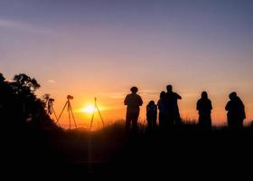 Los turistas de silueta se paran mirando la puesta de sol foto