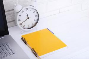 Retro alarm clock with notebook near brick wall on white workplace. Selective focus. Business concept. Copy space photo