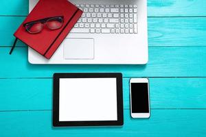 Electronic devices with copy space and keyboard on blue wooden background. Glasses and working accessories. Top view photo