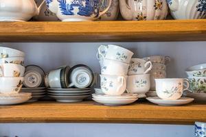 tazas de té con motivos florales de cerámica pintadas a mano con platillos en los estantes foto