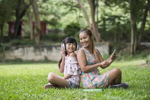 Mother and daughter reading a fairytale to her daughter listen sound with headphone in the park photo