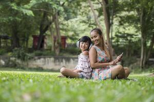 Mother and daughter reading a fairytale to her daughter listen sound with headphone in the park photo