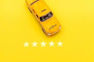 taxi de coche de juguete amarillo y calificación de 5 estrellas aislado sobre fondo amarillo. aplicación de teléfono inteligente del servicio de taxi para buscar en línea llamadas y reservar el concepto de taxi. símbolo de taxi. copie el espacio foto