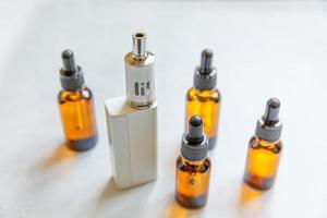 Vaping device e-cigarette electronic cigarette and liquid bottles on concrete stone grey background. Vape device for alternative smoking. Vaping shop concept. Gadget for vaper. Vaping accessories. photo