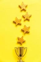 Simply flat lay design winner or champion gold trophy cup and 5 stars rating isolated on yellow background. Victory first place of competition. Winning or success concept. Top view copy space. photo