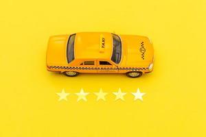 taxi de coche de juguete amarillo y calificación de 5 estrellas aislado sobre fondo amarillo. aplicación de teléfono inteligente del servicio de taxi para buscar en línea llamadas y reservar el concepto de taxi. símbolo de taxi. copie el espacio foto