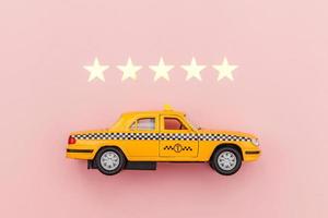 taxi de coche de juguete amarillo y calificación de 5 estrellas aislado sobre fondo rosa. aplicación de teléfono inteligente del servicio de taxi para buscar en línea llamadas y reservar el concepto de taxi. símbolo de taxi. copie el espacio foto