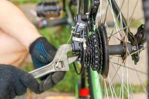 Bike mechanic man repairs bicycle in bicycle repair shop, outdoor. Hand of cyclist bicyclist examines, fixes modern cycle transmission system. Bike maintenance, sport shop concept. photo